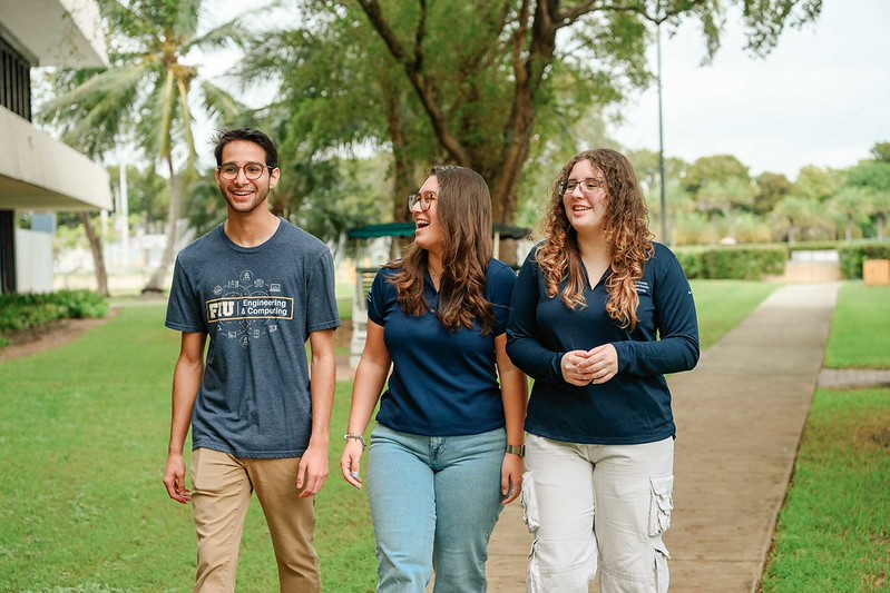Three students walking alongside each other smiling 