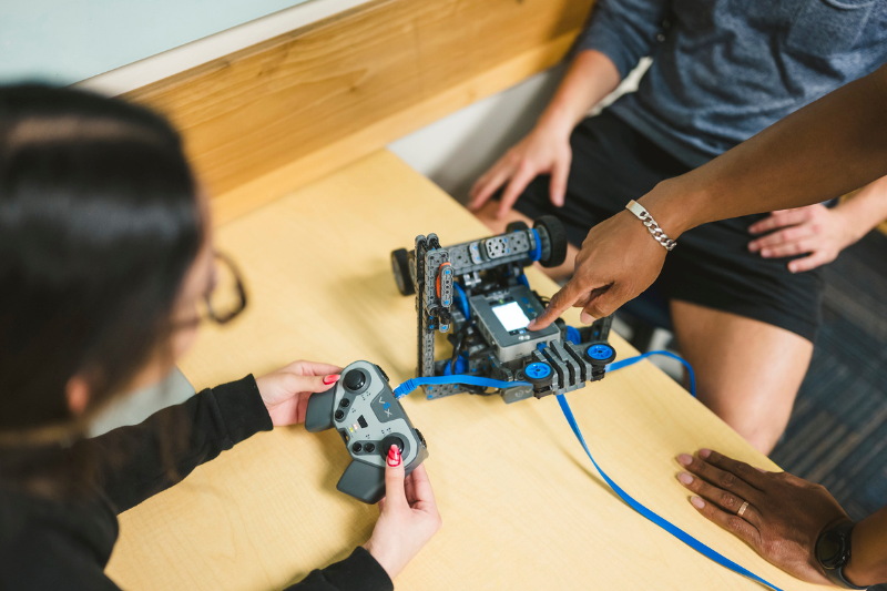 Individual pointing at a piece of a robot explaining to students