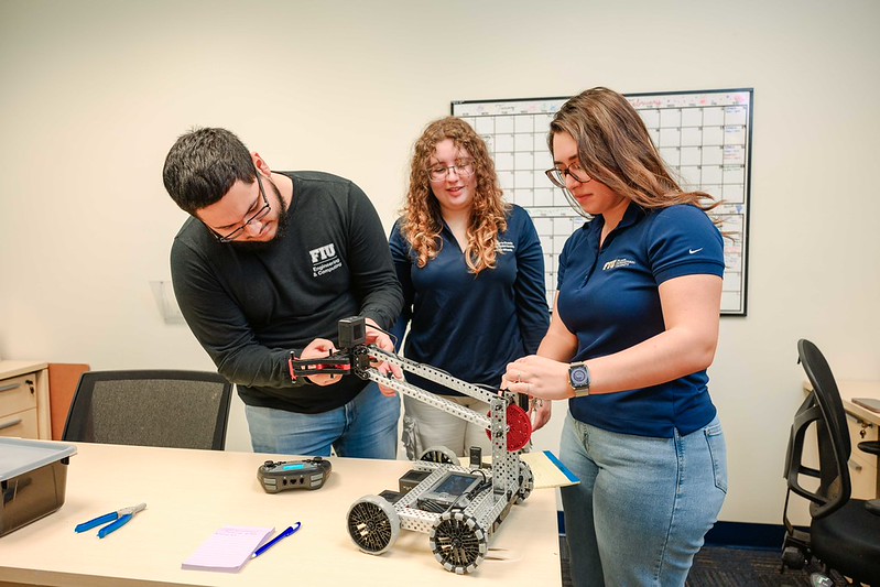 Three students working on programming and adjusting a robot
